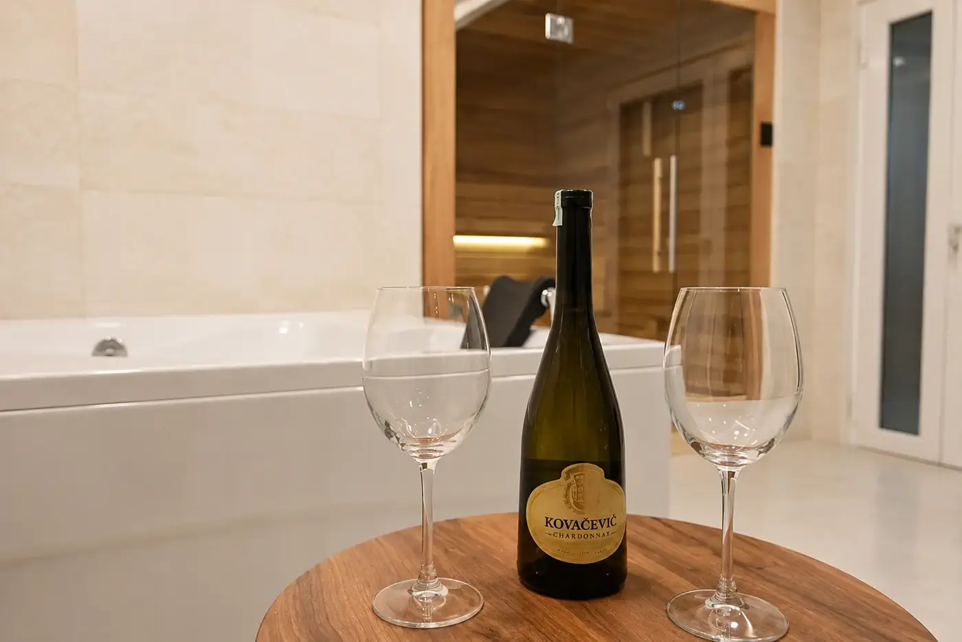 Chilled bottle of Chardonnay and two glasses beside a hot tub and timber sauna