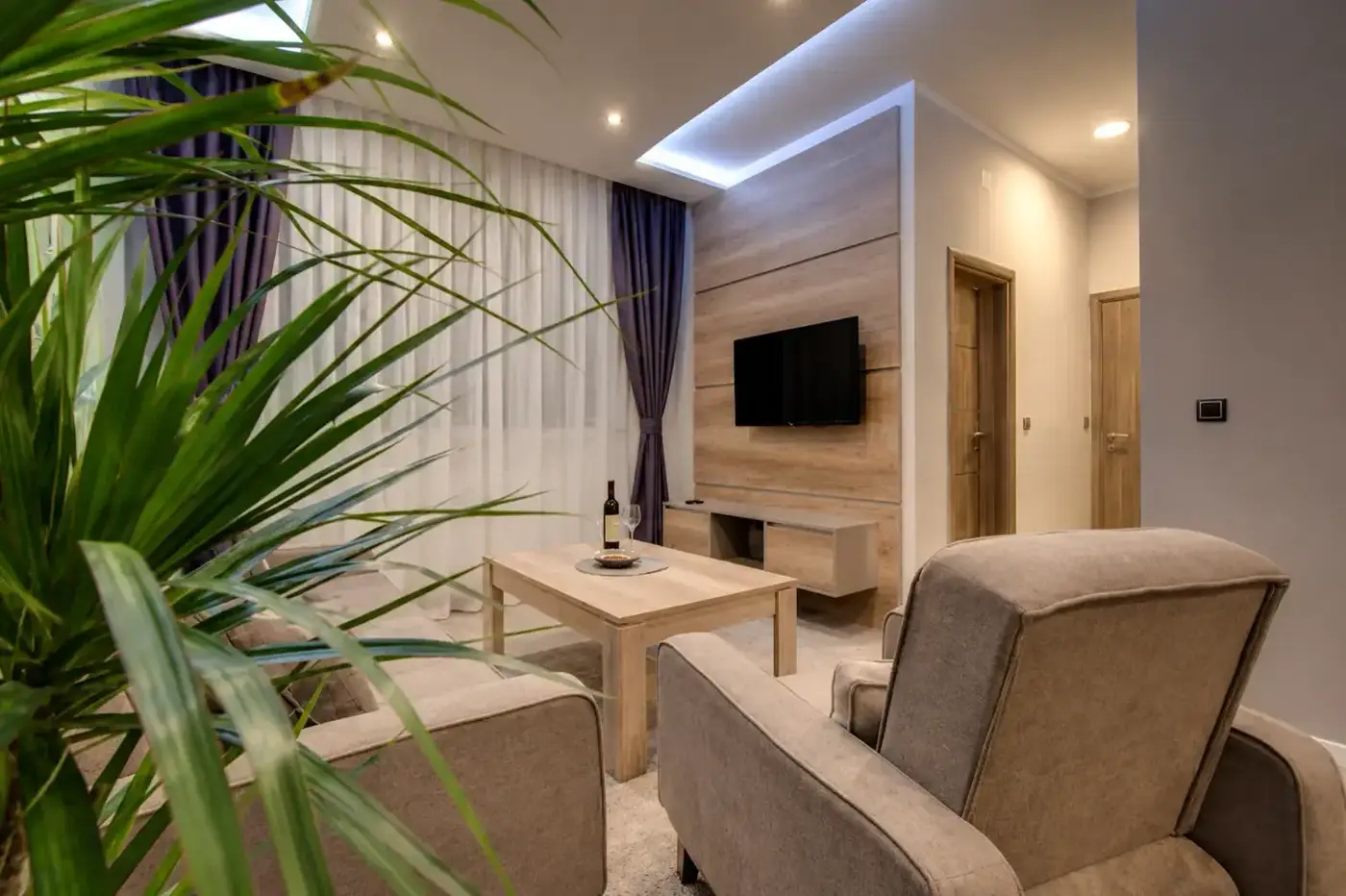 Apartment sitting area with armchairs, a timber media wall and wine on the table